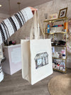 Person holding a beige tote bag with a design on a desk with stationery items