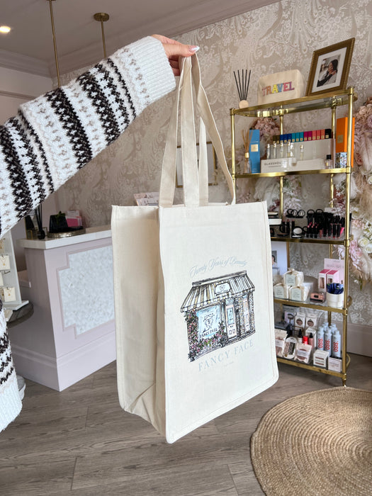 Person holding a beige tote bag with a design on a desk with stationery items