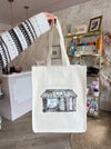 Person holding a tote bag with architectural design in a room with decor elements.